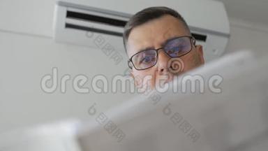 一个戴眼镜的人站在一台工作空调旁边，正在学习该装置的说明书。